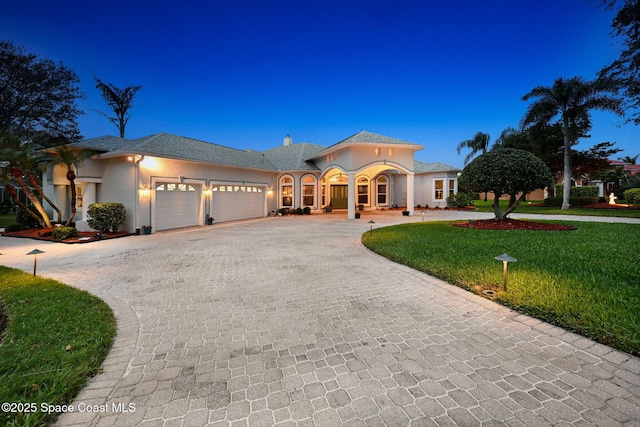 view of front facade with decorative driveway, a chimney, stucco siding, an attached garage, and a front yard