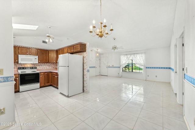 kitchen featuring white appliances, vaulted ceiling with skylight, light tile patterned floors, and ceiling fan with notable chandelier