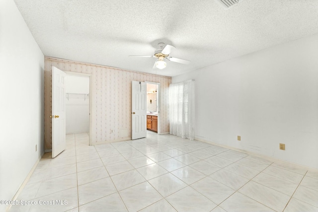 empty room featuring ceiling fan, light tile patterned floors, and a textured ceiling