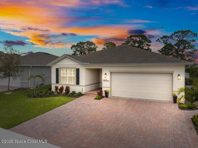 single story home with decorative driveway, an attached garage, a lawn, and stucco siding