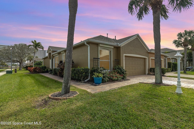 view of front of house featuring an attached garage, a yard, decorative driveway, and stucco siding