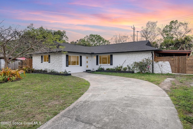 single story home with stone siding, driveway, a shingled roof, and a yard