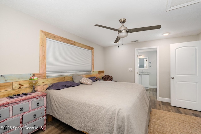 bedroom featuring dark wood-style floors, ensuite bathroom, visible vents, baseboards, and ceiling fan