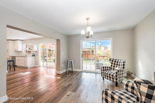 living area featuring baseboards, a chandelier, light wood-style flooring, and a textured ceiling