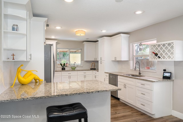 kitchen featuring stainless steel appliances, a sink, a peninsula, white cabinetry, and open shelves