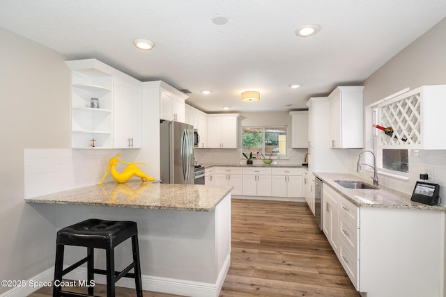 kitchen with white cabinetry, a sink, open shelves, appliances with stainless steel finishes, and a peninsula