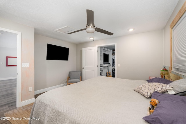 bedroom featuring a ceiling fan, wood finished floors, attic access, baseboards, and a textured ceiling