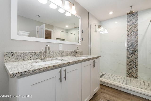 bathroom featuring double vanity, wood finished floors, a sink, and a stall shower