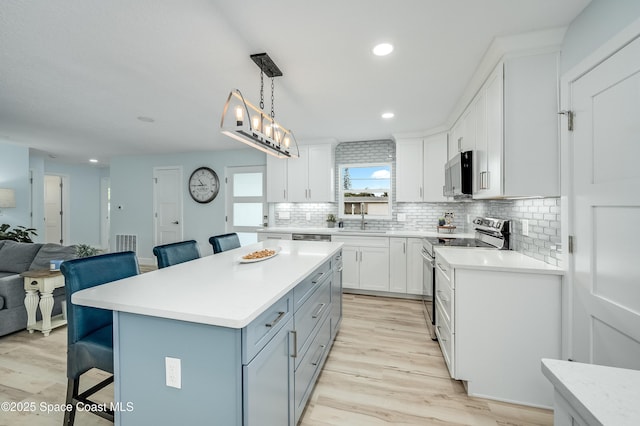 kitchen with stainless steel appliances, white cabinets, light countertops, and a kitchen bar