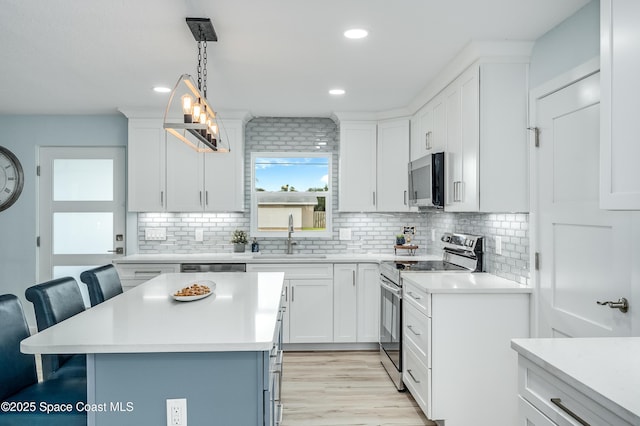 kitchen featuring a breakfast bar area, light countertops, stainless steel appliances, pendant lighting, and a sink