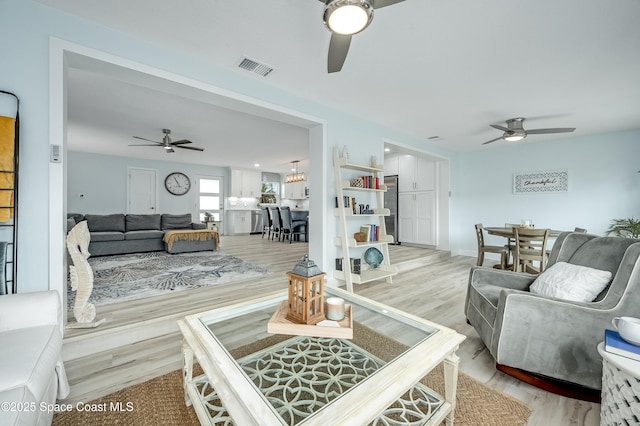 living room with light wood-type flooring, visible vents, and a ceiling fan