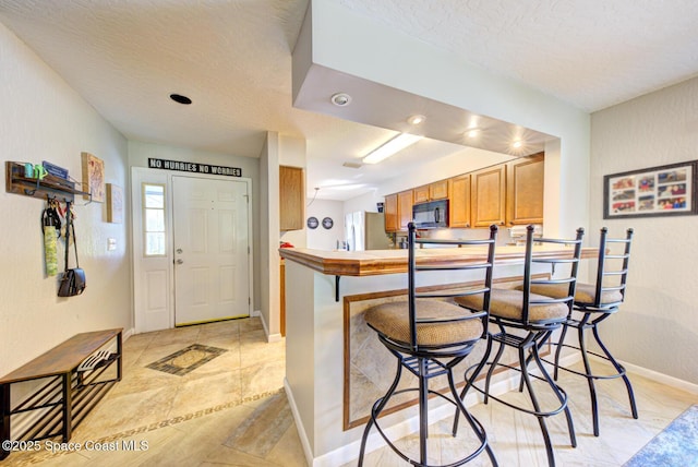 kitchen with brown cabinets, freestanding refrigerator, black microwave, a peninsula, and baseboards