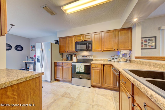 kitchen featuring brown cabinets, light countertops, visible vents, appliances with stainless steel finishes, and a textured ceiling