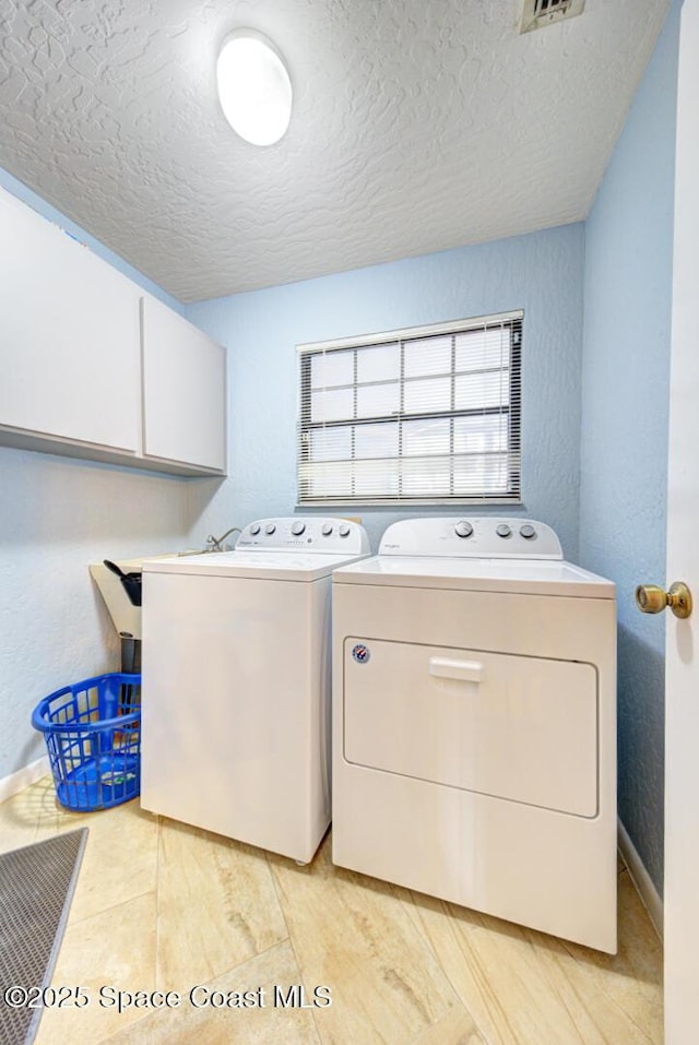 washroom with cabinet space, a textured wall, a textured ceiling, and separate washer and dryer