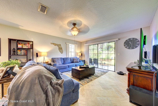 living room with a textured ceiling, a textured wall, visible vents, and a ceiling fan