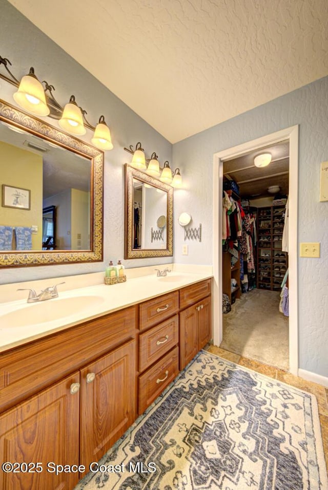 full bathroom featuring double vanity, a textured wall, a spacious closet, a textured ceiling, and a sink