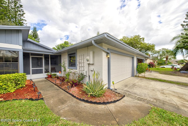 exterior space with an attached garage, a sunroom, concrete driveway, and stucco siding