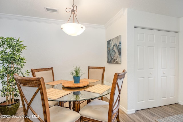 dining room featuring baseboards, light wood-type flooring, visible vents, and crown molding