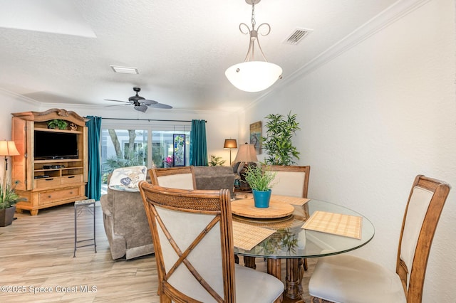 dining room featuring ornamental molding, visible vents, a textured ceiling, and light wood finished floors