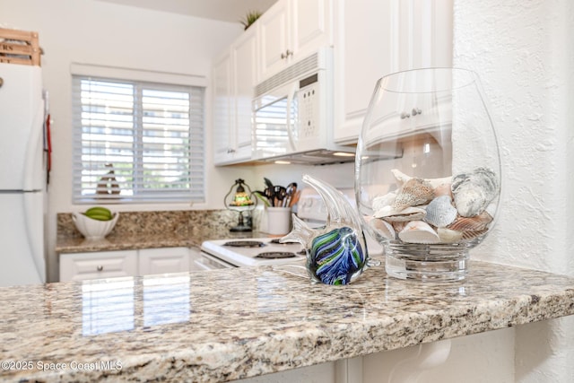 kitchen featuring a textured wall, light stone counters, white appliances, and white cabinetry