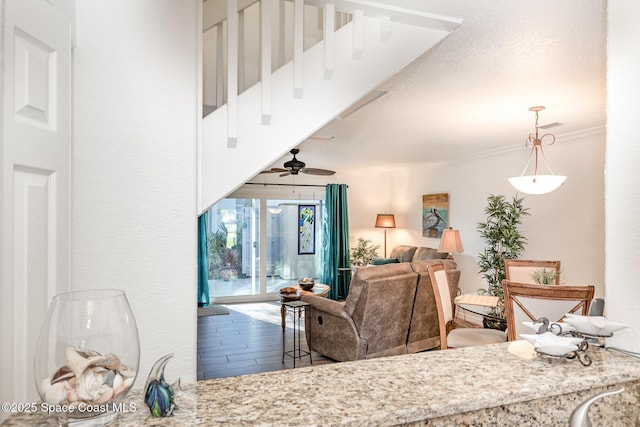 living area featuring a textured wall, ceiling fan, ornamental molding, wood finished floors, and a textured ceiling