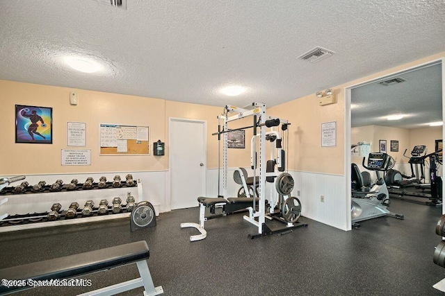 gym with a wainscoted wall, visible vents, and a textured ceiling