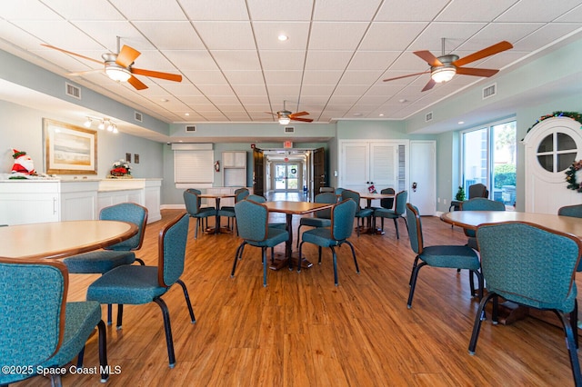 dining area featuring light wood finished floors, baseboards, visible vents, and a drop ceiling