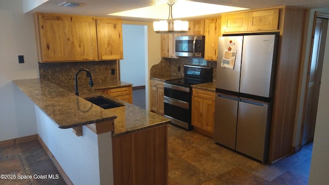 kitchen featuring visible vents, appliances with stainless steel finishes, a sink, dark stone countertops, and a peninsula