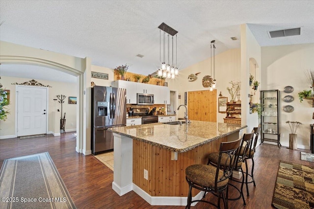 kitchen featuring stainless steel appliances, hanging light fixtures, white cabinets, a sink, and an island with sink