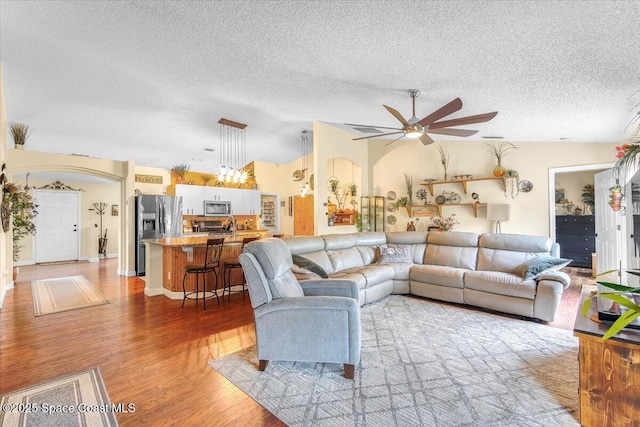 living room featuring arched walkways, lofted ceiling, light wood-style flooring, a ceiling fan, and a textured ceiling