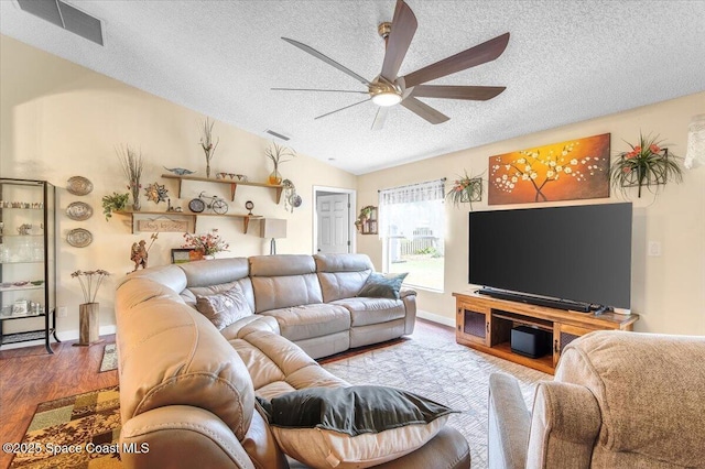 living room featuring lofted ceiling, a textured ceiling, wood finished floors, visible vents, and a ceiling fan