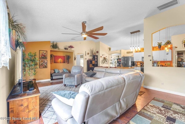 living area featuring ceiling fan, a textured ceiling, light wood-style flooring, visible vents, and vaulted ceiling