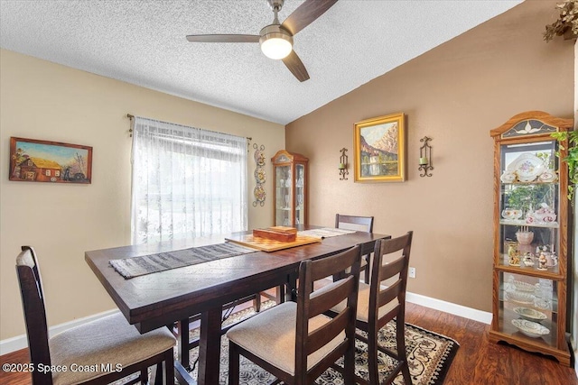 dining room with baseboards, a ceiling fan, lofted ceiling, dark wood-style flooring, and a textured ceiling