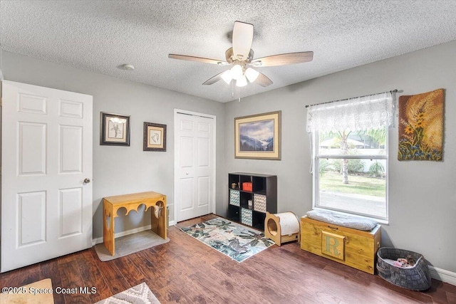 living area with ceiling fan, a textured ceiling, baseboards, and dark wood-type flooring