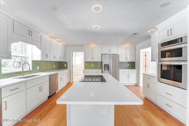 kitchen with sink, a center island, white cabinetry, light hardwood / wood-style floors, and stainless steel appliances