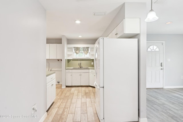 kitchen featuring decorative light fixtures, light countertops, freestanding refrigerator, white cabinetry, and a sink