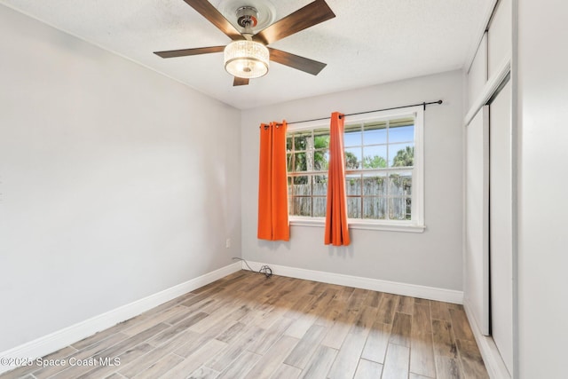 unfurnished bedroom featuring a ceiling fan, a closet, light wood-style flooring, and baseboards