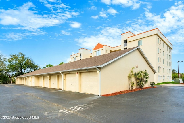 view of side of home with stucco siding, a shingled roof, and community garages