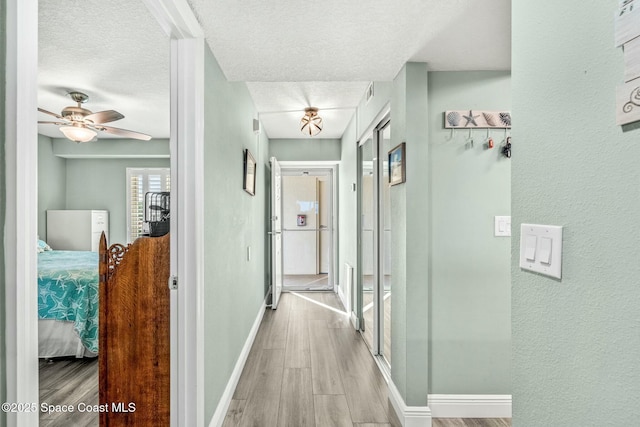 hall featuring light wood-type flooring, a textured ceiling, and baseboards