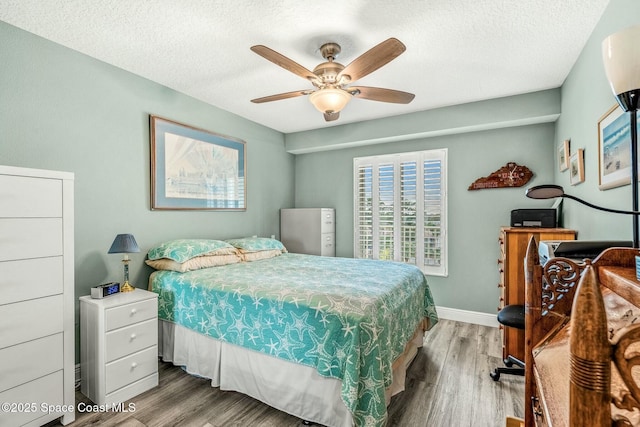 bedroom with a textured ceiling, ceiling fan, wood finished floors, and baseboards