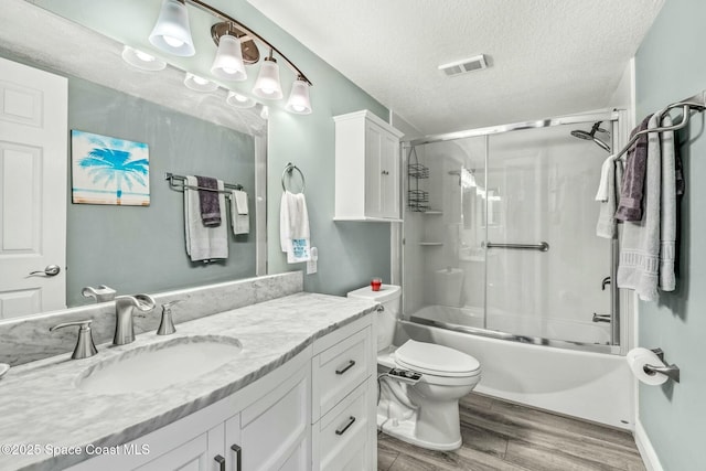 bathroom with a textured ceiling, bath / shower combo with glass door, wood finished floors, visible vents, and vanity