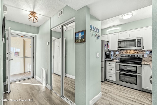 kitchen with tasteful backsplash, visible vents, appliances with stainless steel finishes, light wood-style floors, and white cabinetry