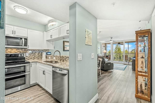 kitchen with appliances with stainless steel finishes, white cabinets, a sink, and light stone countertops