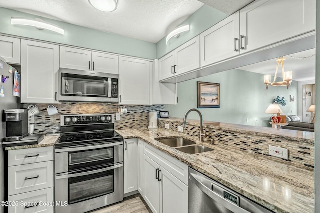 kitchen with stainless steel appliances, a sink, white cabinetry, decorative backsplash, and decorative light fixtures