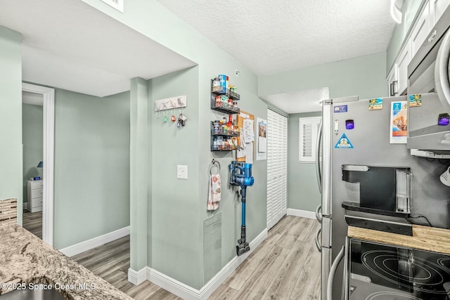 kitchen featuring light wood finished floors, baseboards, appliances with stainless steel finishes, and a textured ceiling