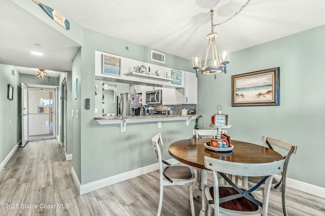 dining space with visible vents, an inviting chandelier, a textured ceiling, light wood-type flooring, and baseboards