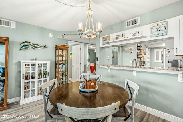 dining area featuring a chandelier, visible vents, baseboards, and wood finished floors