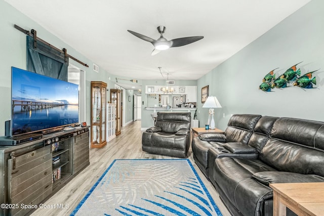 living room featuring light wood-style floors, visible vents, and ceiling fan with notable chandelier