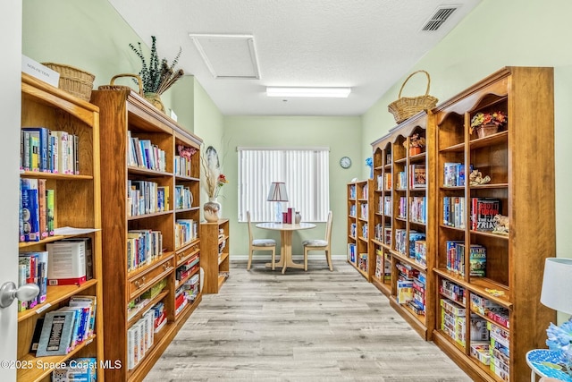 living area with visible vents, baseboards, a textured ceiling, light wood-style floors, and bookshelves