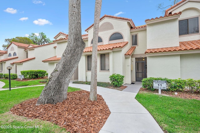 mediterranean / spanish-style house featuring a tiled roof, a front lawn, and stucco siding